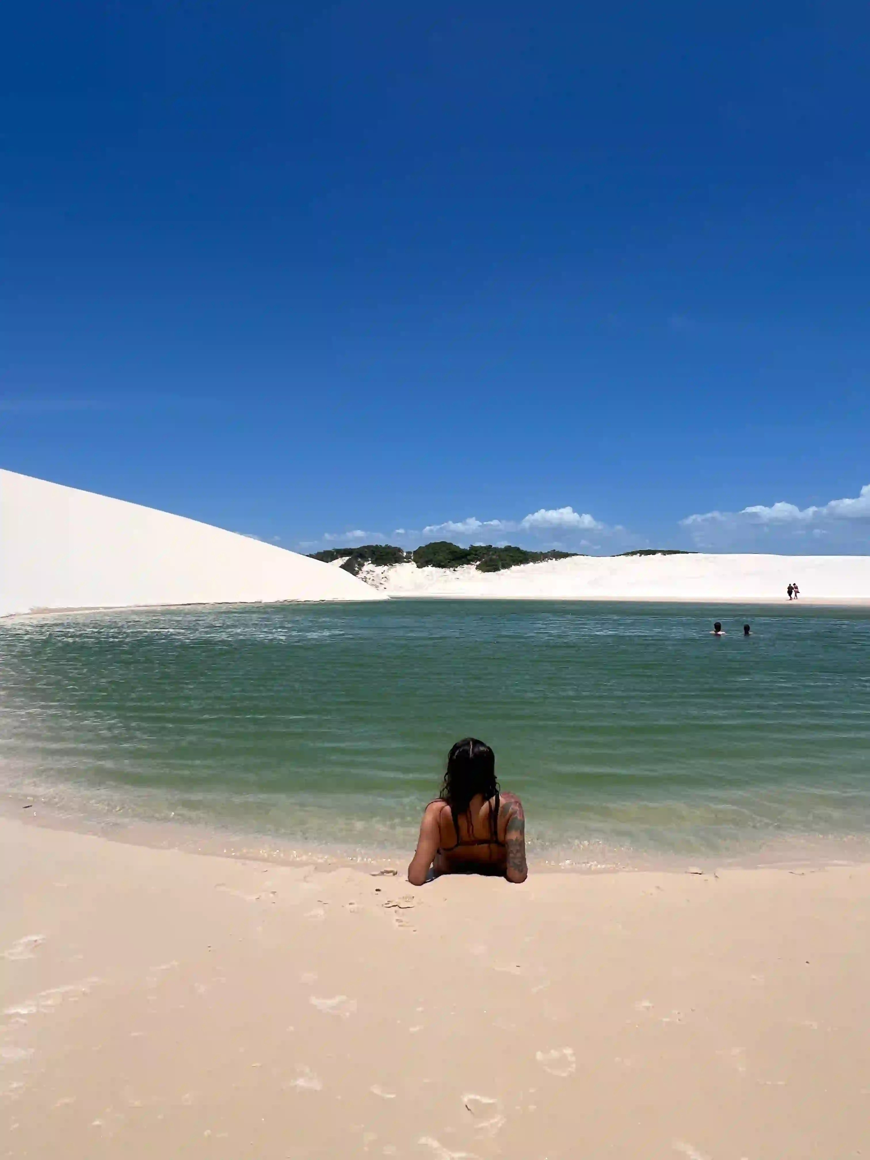 A woman relaxing near a green lagoon in Lencois Maranhenses, Brazil